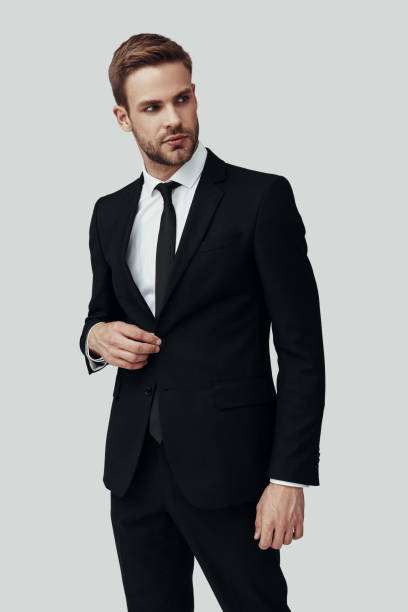 istock Handsome young man in formalwear looking away and adjusting jacket while standing against grey background 1170880876