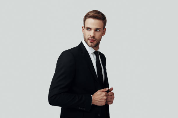 istock Handsome young man in formalwear looking away and adjusting jacket while standing against grey background 1170881596