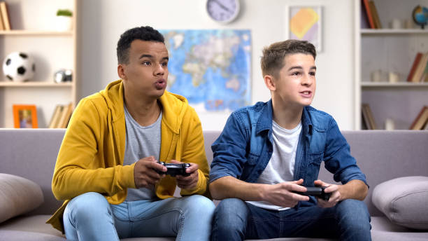 возбужденные многоэтнические друзья-подростки, наслаждающиеся видеоиграми, свободное время дома - video game friendship teenager togetherness стоковые фото и изображения