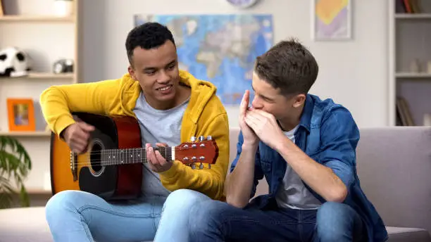 Multiracial teenage friends playing guitar and mouthorgan hobby musician career