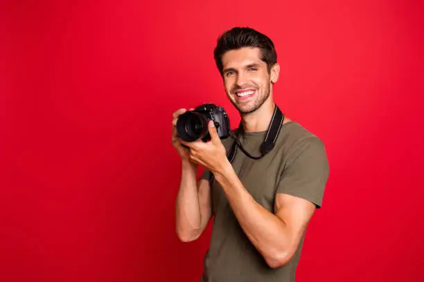 Photo of Photo of amazing guy with photo digicam making creative shots wear casual grey t-shirt isolated on red background