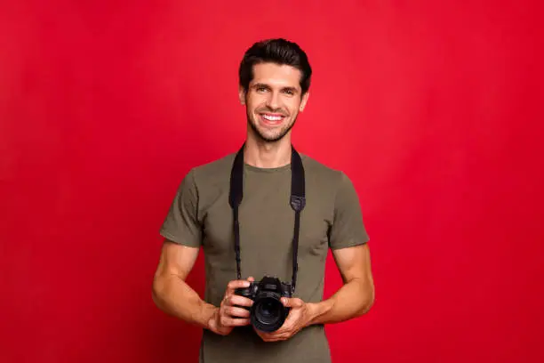 Photo of Photo of amazing guy with photo digicam in hands wear casual grey t-shirt isolated on red background