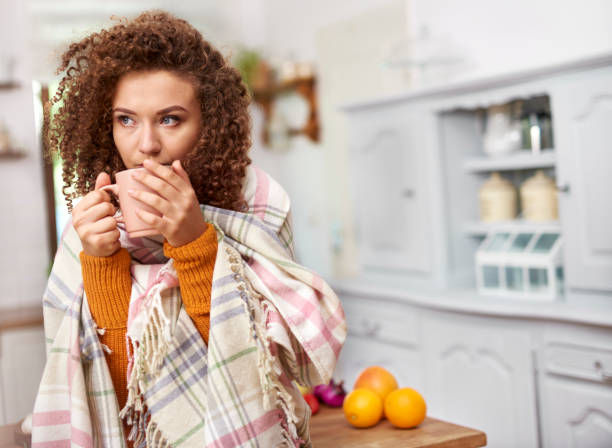 mujer joven envuelta en manta bebiendo té caliente - gripe fotografías e imágenes de stock