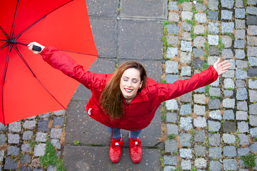 Young woman standing outdoors in the rain, holding red umbrella and eyes closed