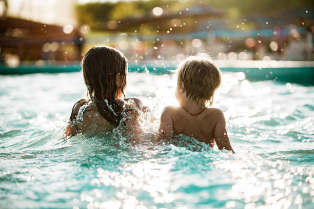 Rear view little boy and girl sitting and splashing in the pool stock photo