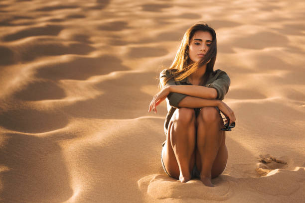 Beautiful young woman sitting on a sand dune