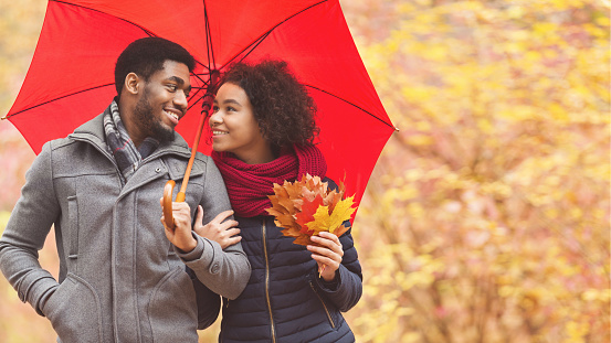 Family walk. Afro couple under umbrella at rainy day, dating in park, copy space