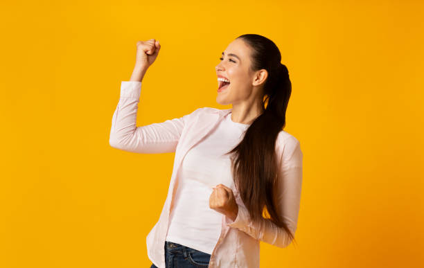 ragazza eccitata che scuote i pugni celebrando la vittoria su sfondo giallo - women standing fist success foto e immagini stock