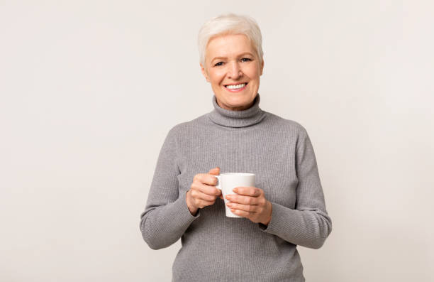 istock Elderly lady with cup of tea over light studio background 1170926083