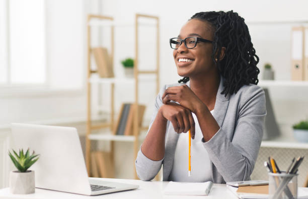 joven afro señora de negocios sonriendo sentado en la oficina moderna - secretary fotografías e imágenes de stock