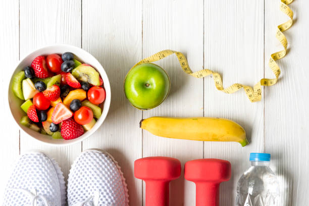 gesunder lebensstil für frauen ernährung mit hanteln sportgeräte, turnschuhe, maßband, obst gesunde grüne äpfel und flasche wasser auf holz.  gesundes konzept. - fitness trainer stock-fotos und bilder