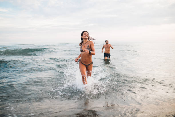 pareja juguetona disfrutando del mar - swimming trunks bikini swimwear red fotografías e imágenes de stock