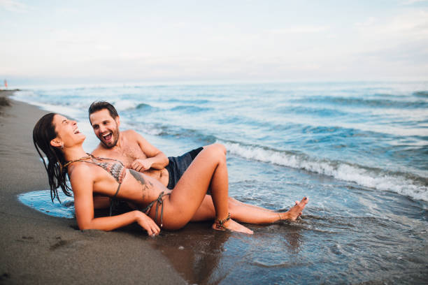 joven pareja tumbada en la playa y divirtiéndose - swimming trunks bikini swimwear red fotografías e imágenes de stock