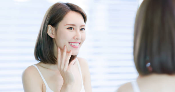 Young asian woman look mirror Young asian skin care woman smile and look mirror cheek photos stock pictures, royalty-free photos & images
