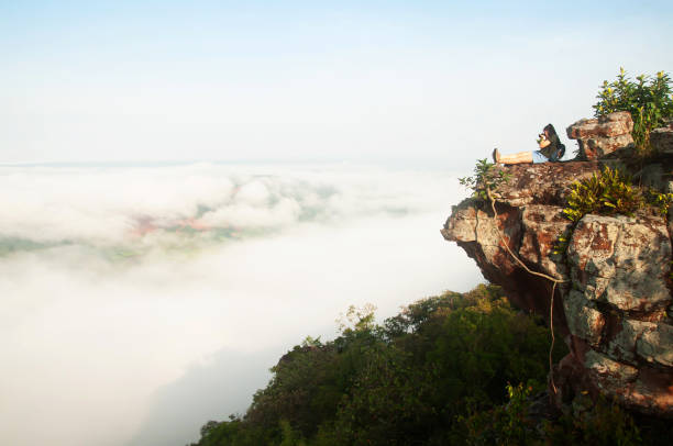 istock Young woman seating on a precipice while enjoying morning mist view with camera. 1170953660