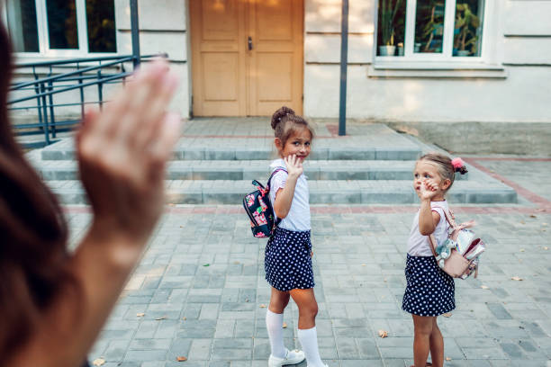 istock Young mother waving to her daughters before classes outdoors primary school seeing them off. Family saying goodbye. 1170959580