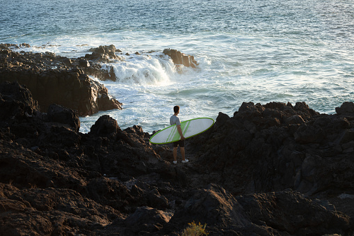 A surfer walks along a rocky coast in Portugal