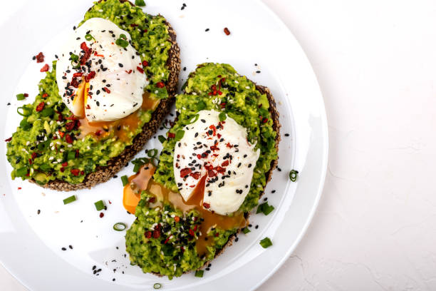 istock Poached eggs with avocado guacomole on brown bread with sesame seeds. Healthy breakfast on a white background. 1170966403