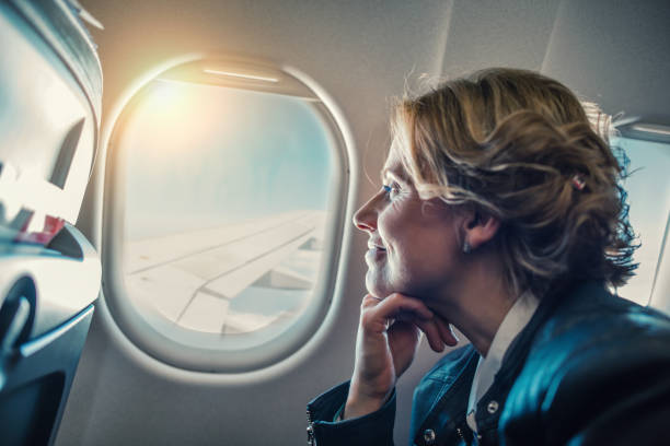 frau schaut durch fenster im flugzeug - fensterplatz fahrzeugsitz stock-fotos und bilder