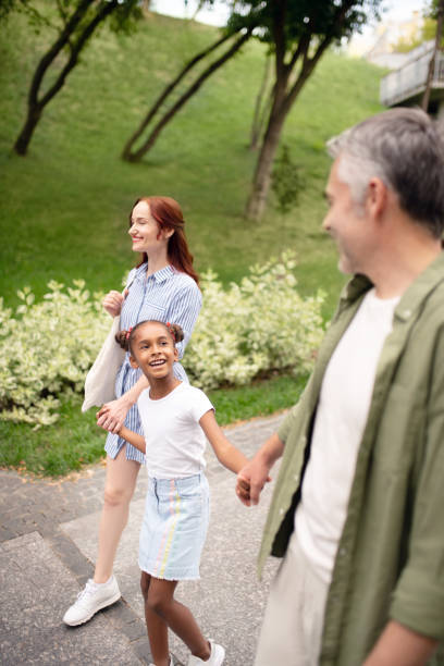 istock Beautiful adopted girl talking to daddy while walking with parents 1170967673