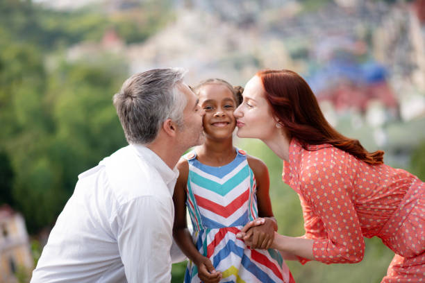 padres adoptivos besando a su linda chica de piel oscura - pareja acogido al aire libre fotografías e imágenes de stock