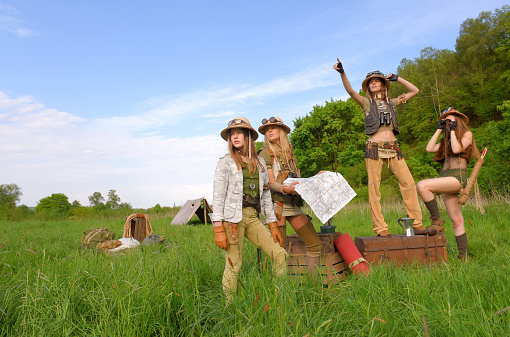 Four young female globetrotters get together as explorers.
They set up a tented camp in the outdoor wilderness. They 
dress up with safari hats and safari clothing.