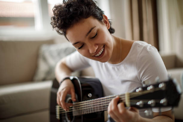 istock Smiling young woman playing a guitar at home 1170984049