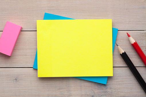 Yellow note with empty place for your text with pencil and eraser aside on wooden desk. Reminder concept.