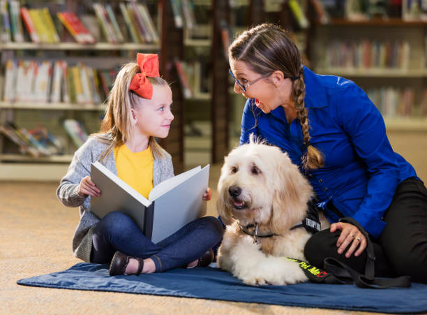 istock Girl in library reading with therapy dog and trainer 1170987857