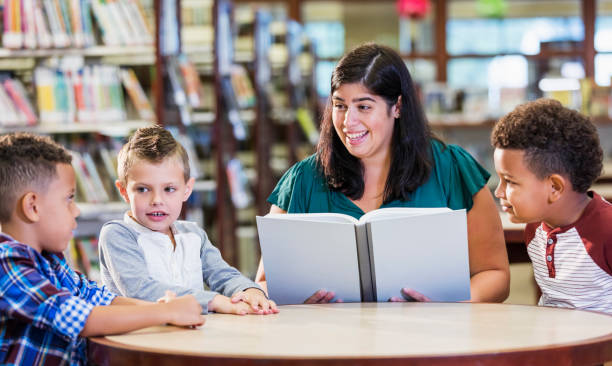 istock Hispanic teacher with three boys in library reading book 1170987906