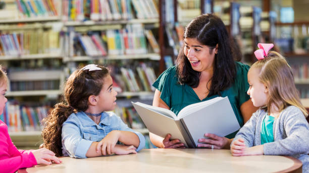 istock Hispanic teacher and three girls in library reading book 1170988619
