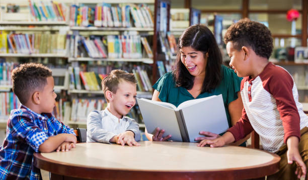 istock Hispanic teacher with three boys in library reading book 1170988689