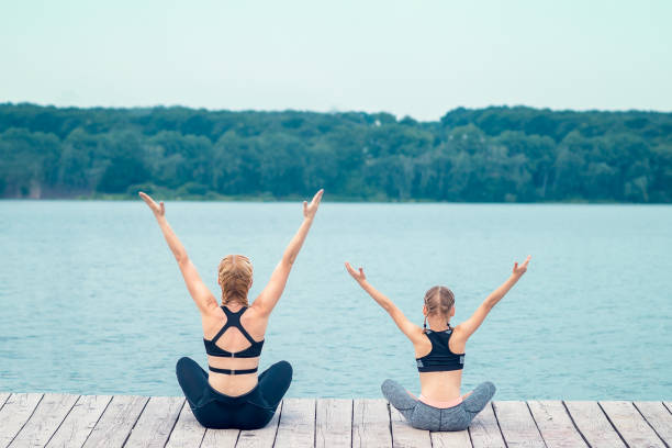 istock mother and daughter practicing yoga on a pier 1170989627
