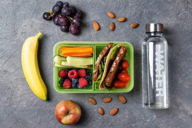 schule lunchbox mit sandwich, gemüse, obst und wasser auf schwarzem hintergrund, gesunde ernährung konzept, top-ansicht - lunch box lunch sandwich green stock-fotos und bilder
