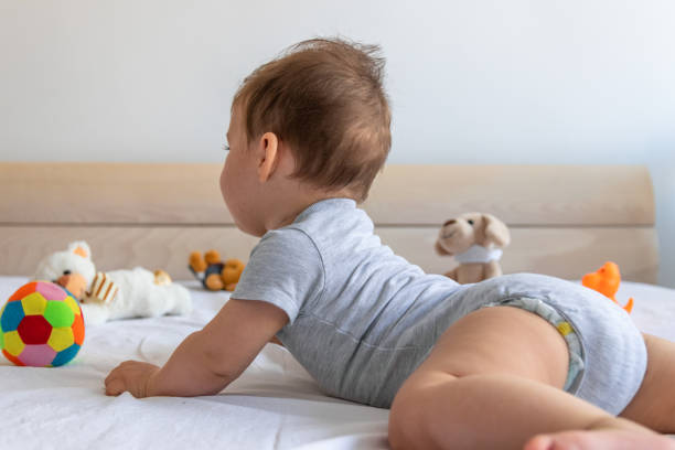 bébé rampant dans le lit pour attraper ses jouets - être étendu sur le ventre photos et images de collection