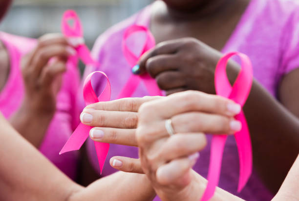 Multi-ethnic women with breast cancer awareness ribbons Cropped view of four multi-ethnic women wearing pink shirts, holding breast cancer awareness ribbons. The focus is on one of the hands. breast cancer stock pictures, royalty-free photos & images