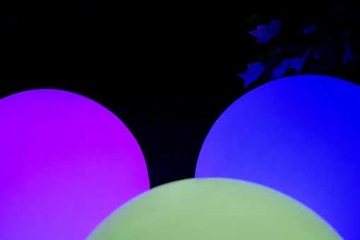Fragments of three purple, light green and blue balls glowing in three colors and a dark branch in the dark.