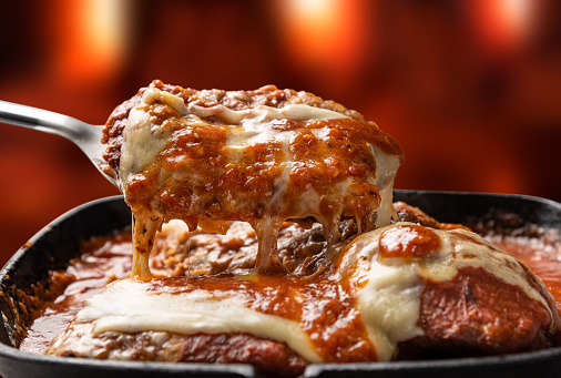 Parmegiana Steak aislado también conocido como Filet Parmegiana en una sartén de hierro negro sobre un fondo de fuego de madera fuera de foco, queso y salsa de tomate. photo