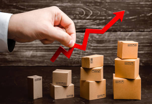 Businessman holds a red arrow up above cardboard boxes folded incrementally. Increase sales and production rate of goods and products. Profit growth, business development. Increase in export volumes. el hombre de negocios sostiene una flecha roja arriba por encima de las cajas de cartón dobladas gradualmente. aumentar la tasa de ventas y producción de bienes y productos. crecimiento de beneficios, desarrollo de negocios. aumento de los volúmenes de