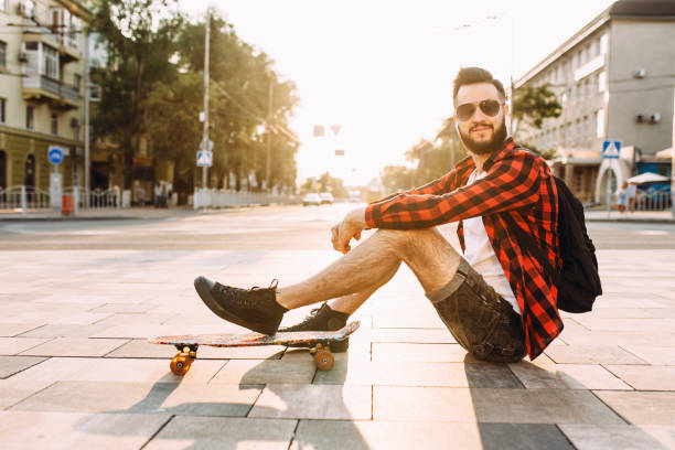istock guy with a beard in wireless headphones sits in a park with a skateboard 1171025021