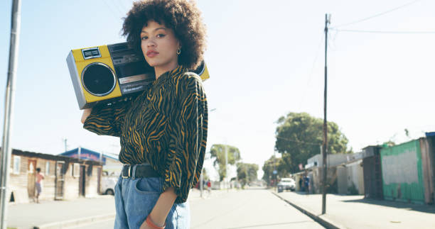 Listening to the sounds of the streets Shot of an attractive young woman listening to music on a boombox in an urban setting retro fashion stock pictures, royalty-free photos & images