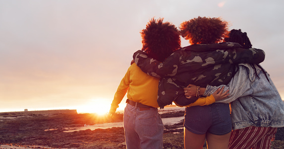 Rearview shot of a group of young women embracing on the beach at sunset