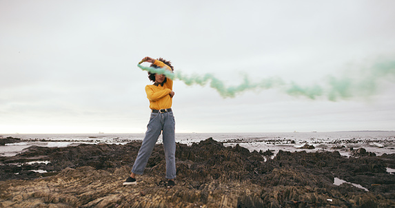 Shot of an attractive young woman waving a green flare on the beach