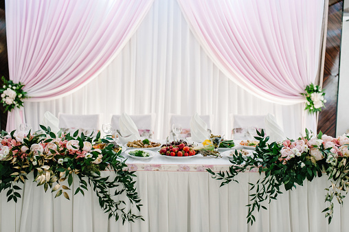 Festive table decorated with composition of pink flowers and greenery in the banquet hall. Table newlyweds in the banquet area on wedding party.