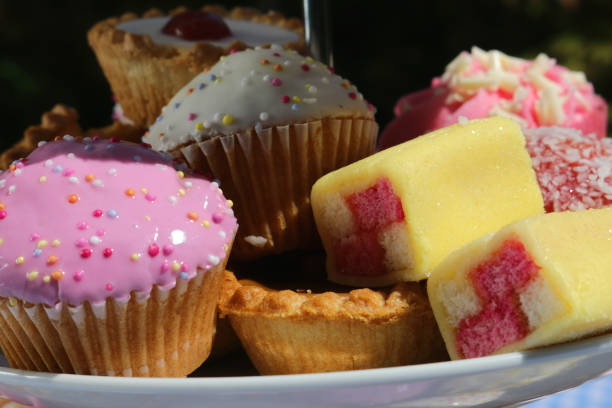 primer plano del picnic buffet de té de la tarde de pasteles cupcakes en soporte de pastel escalonado de porcelana blanca con tres niveles en mantel azul a cuadros en la fiesta del jardín, tartas de pastel de cereza, magdalenas de chocolate, pastel batte - fondant fancies fotografías e imágenes de stock