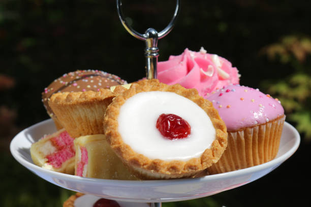 imagem do piquenique do bufete do chá da tarde dos bolos dos queques no carrinho estratificado do bolo da porcelana branca com três camadas no tablecloth checkered azul no partido do jardim, as tortas do bakewell da cereja, muffins do chocolate, bolo cas - fondant fancies - fotografias e filmes do acervo