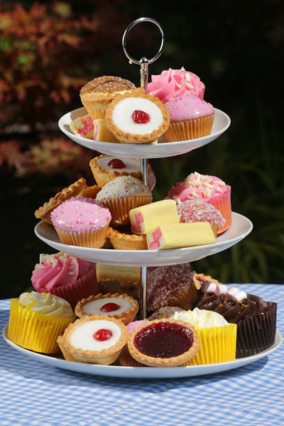 imagen del picnic buffet de té de la tarde de pasteles pastelitos en porcelana blanca soporte de pastel escalonada con tres niveles en mantel azul a cuadros en la fiesta del jardín, tartas de pastel de cereza, magdalenas de chocolate, pastel battenberg c - fondant fancies fotografías e imágenes de stock