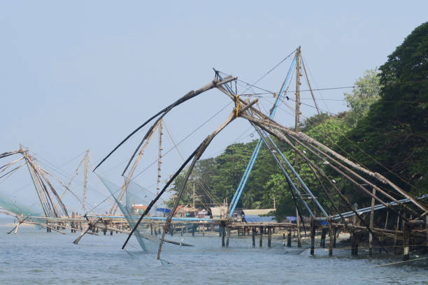 Stock photo of Chinese fishing nets at sunset in Fort Kochi beach in Cochin, Kerala, South India with local Indian fisherman catching tuna fish mackerel from port of Kochi harbour water in Indian Ocean / Arabian Sea, Cheena vala Chinese fishing nets Kochi photo imagen de las redes de pesca chinas al atardecer en la playa de fort kochi en cochin, kerala, al sur de la india con pescador indio local capturando caballa de atún desde el puerto de aguas del puerto de kochi en el océano indico / mar arábigo, cheena v