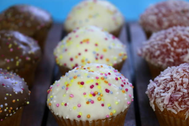 Stock photo of multicolour homemade cupcakes / mini muffins cakes, vanilla, strawberry / raspberry, coconut, chocolate flavours with icing and rainbow sprinkles / hundreds and thousands on top in a row on tray for afternoon tea / children's birthday party food buffet platter