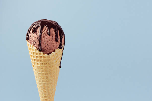 istock Brown ice cream in waffle cone with chocolate sauce on soft light pastel blue background, closeup, half, details, top. 1171059322